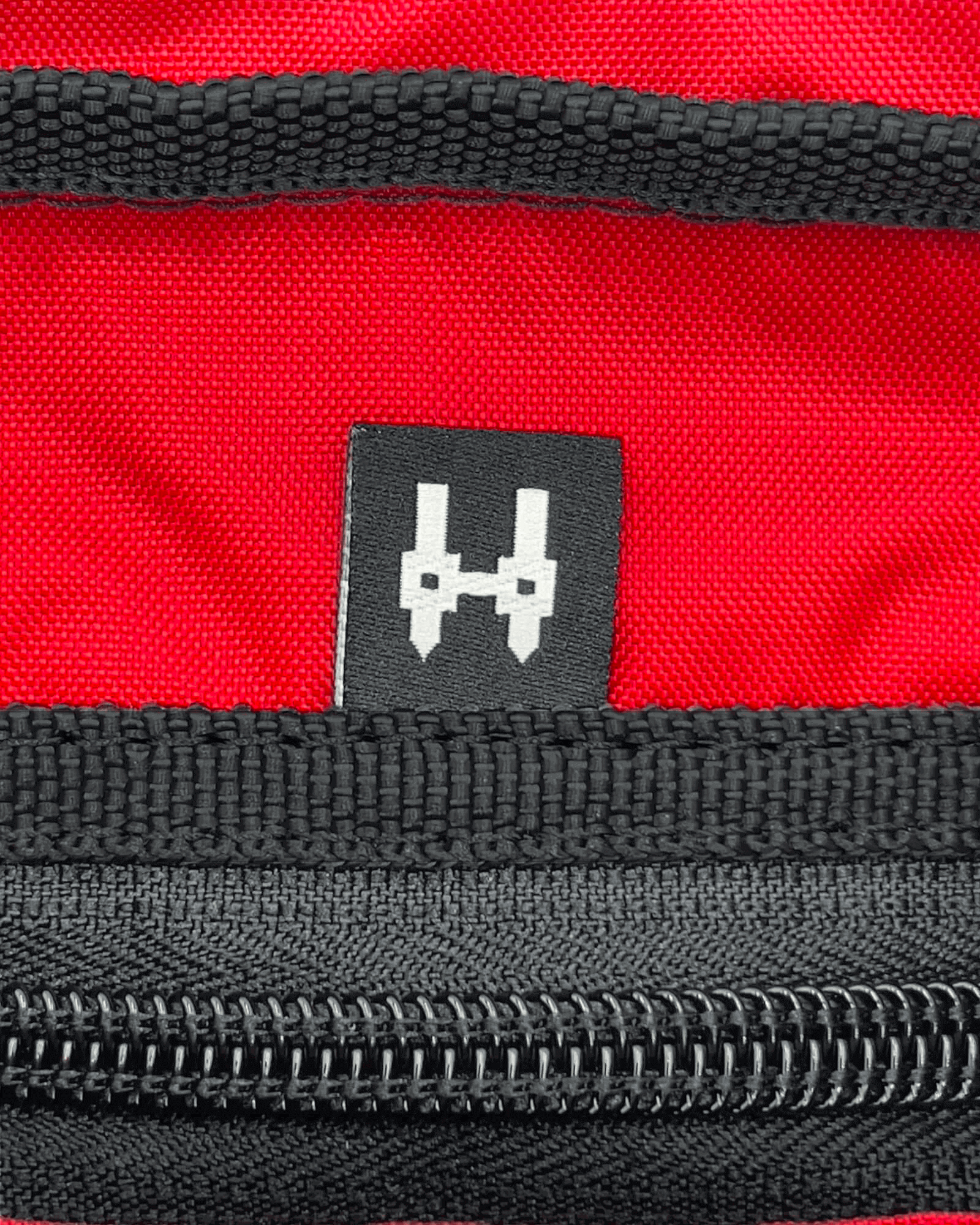 Close-up of a stylish black and silver tag on a red bag, showcasing zipper detail and brand logo.