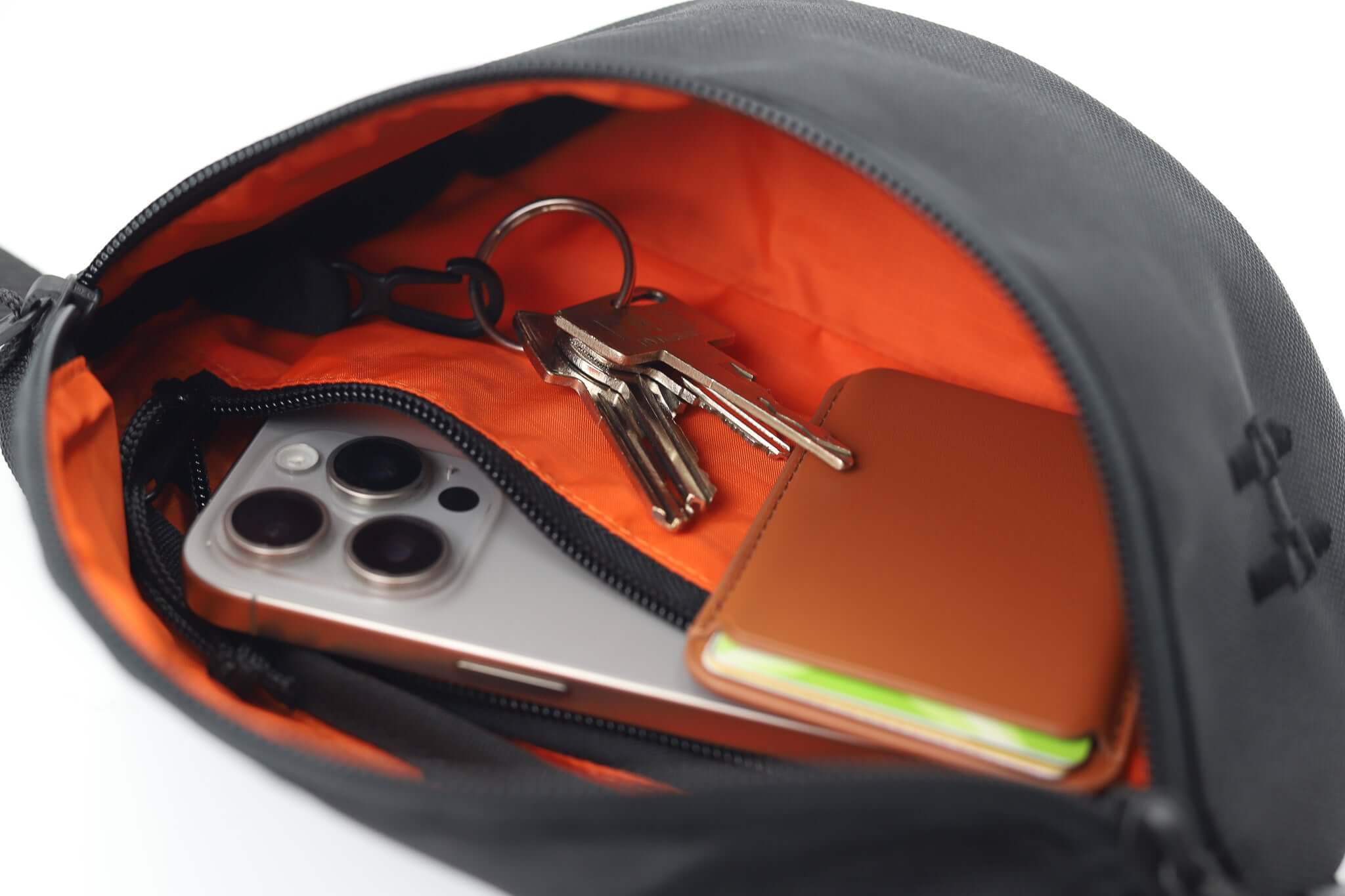 ledvinka Sora 2.0 otevřená s telefonem, klíči a peněženkou na oranžovém pozadí